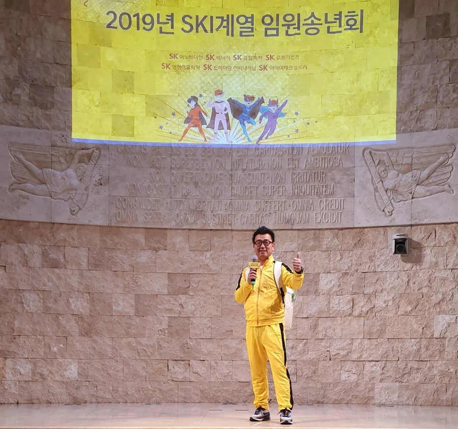 무대 위에서 마이크를 들고 진행하는 사회자, 배경에 행사 안내 슬라이드
