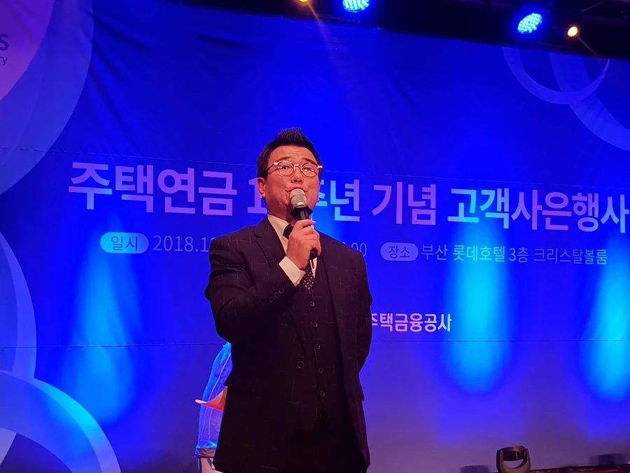 무대 조명 앞에서 정장을 입고 마이크를 들고 진행하는 사회자 클로즈업