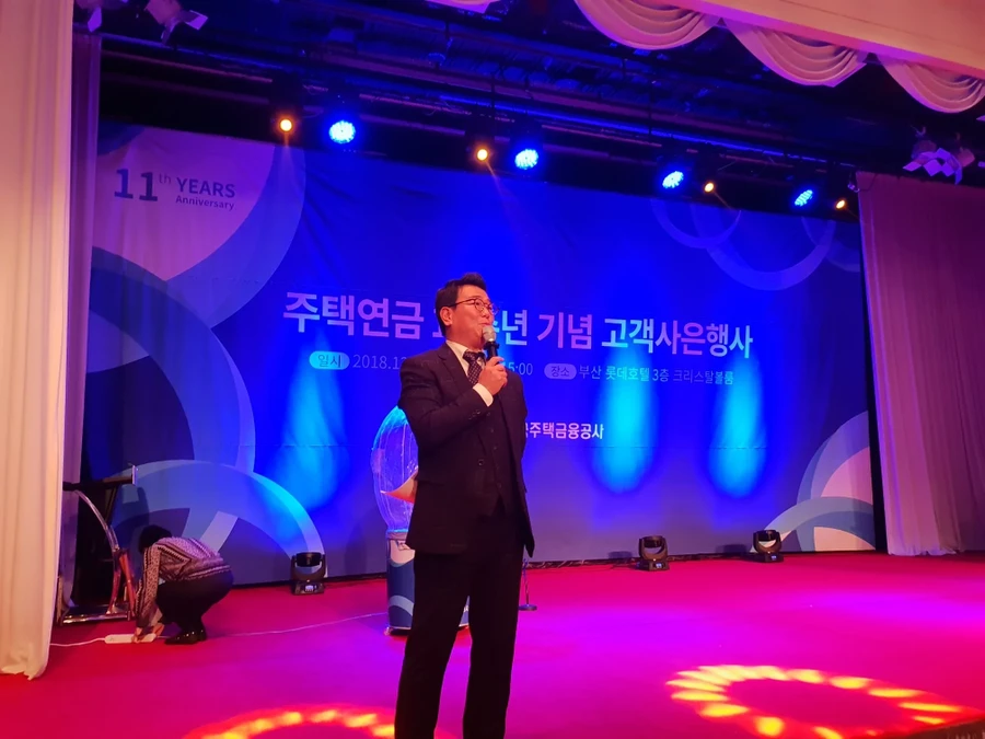 붉은 조명 무대와 커튼 배경 앞에서 마이크를 들고 진행하는 사회자