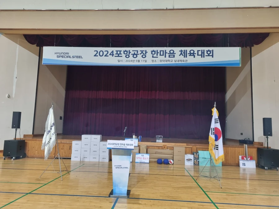 체육관 무대 위 현수막과 연단, 시상품이 정렬된 시상식 준비 장면